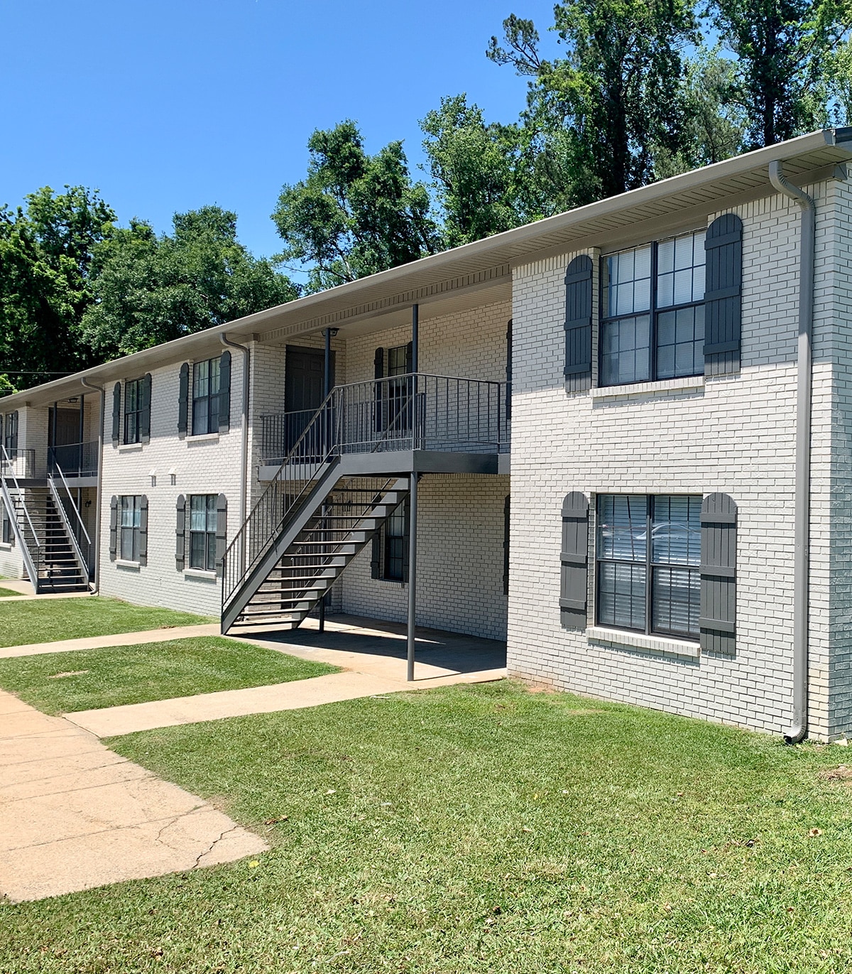 Exterior view of a multi-family residential building with a well-maintained lawn, showcasing available rental properties from Red Rock Realty Group.
